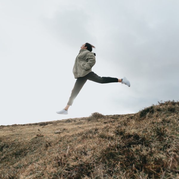 person-jumps-high-with-legs-out-above-a-brown-grassy-hill